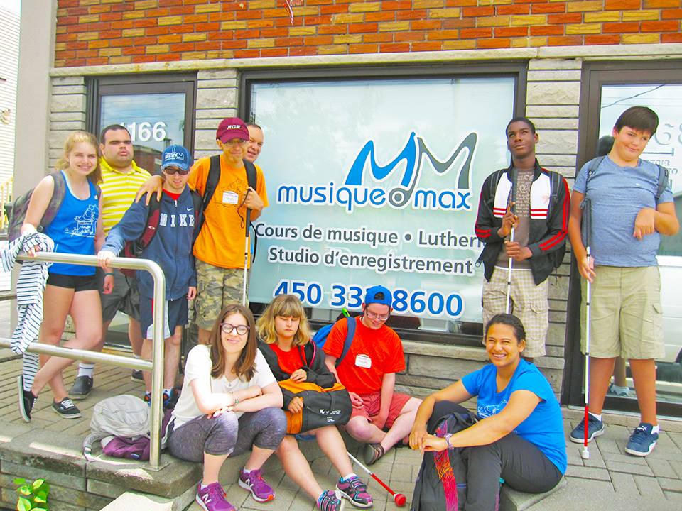 Plusieurs jeunes de la fondation des aveugles assis et debout à l'extérieur devant l'école Musique O Max.