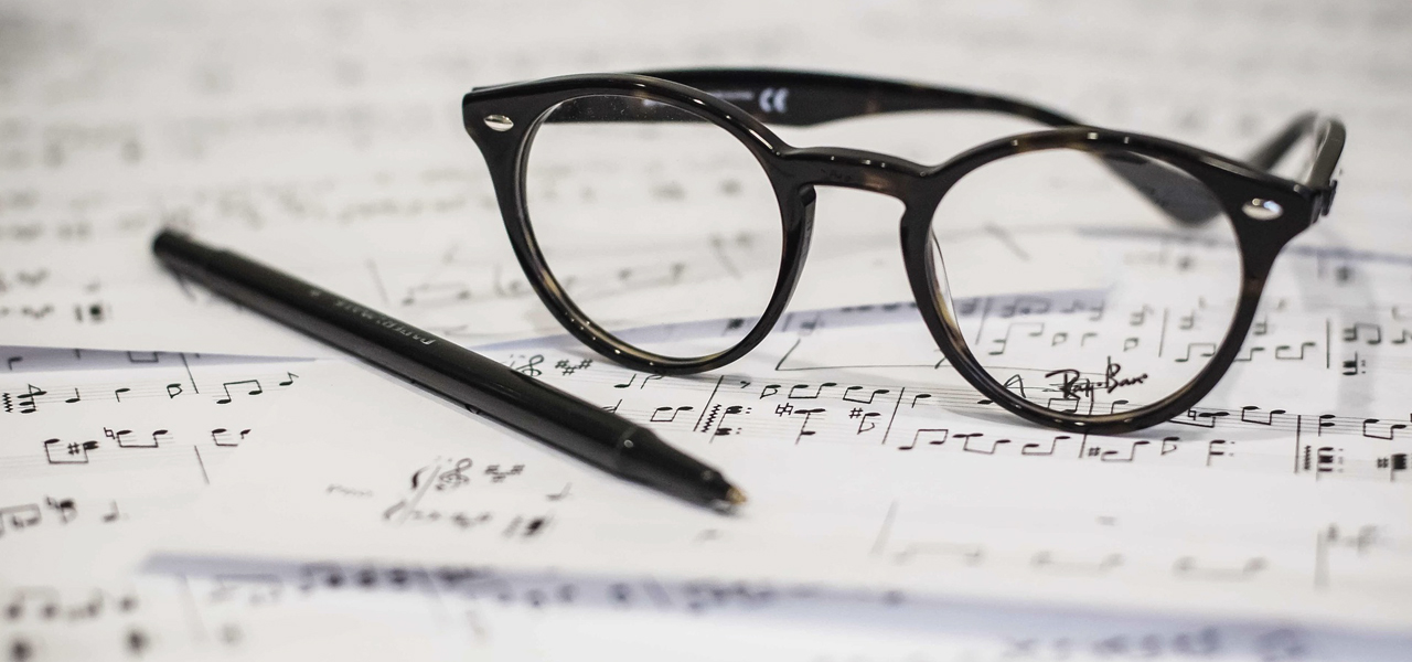 Gros plan d'une feuille de musique avec une paire de lunettes et un crayon sur le dessus.