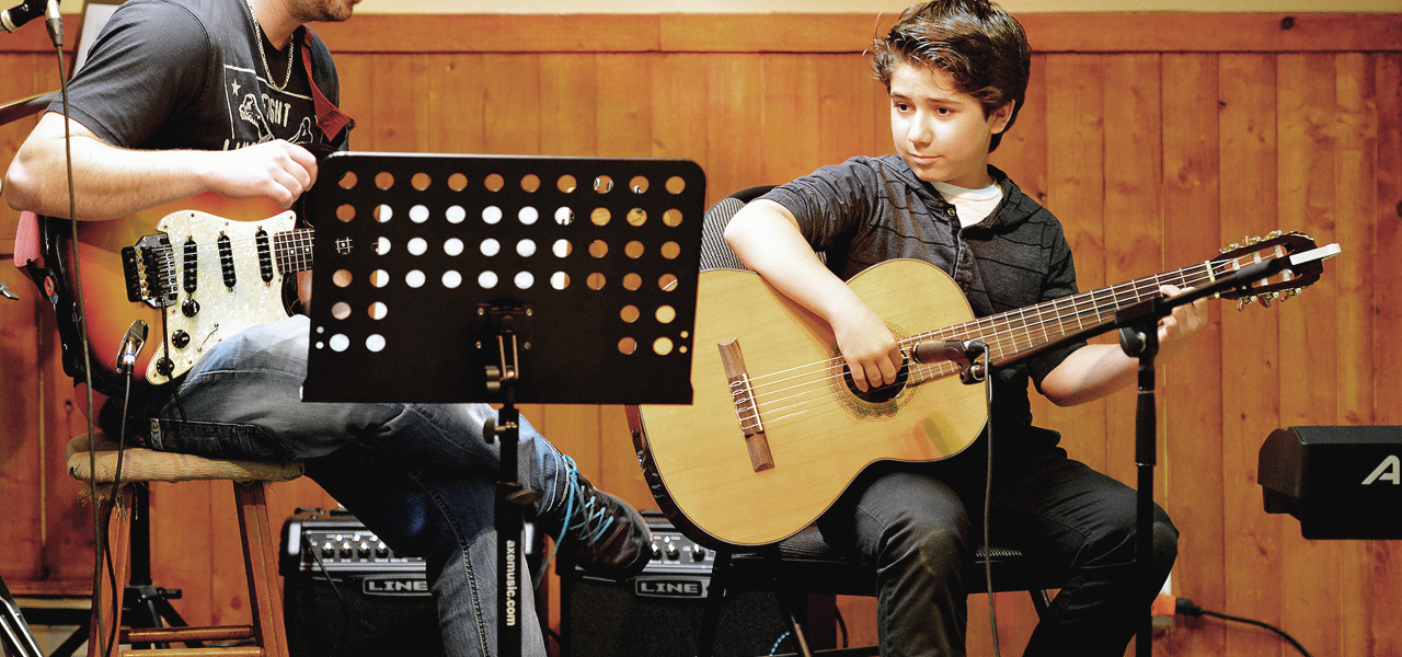 Jeune garçon sur une scène jouant de la guitare lors du spectacle organisé par Musique O Max.