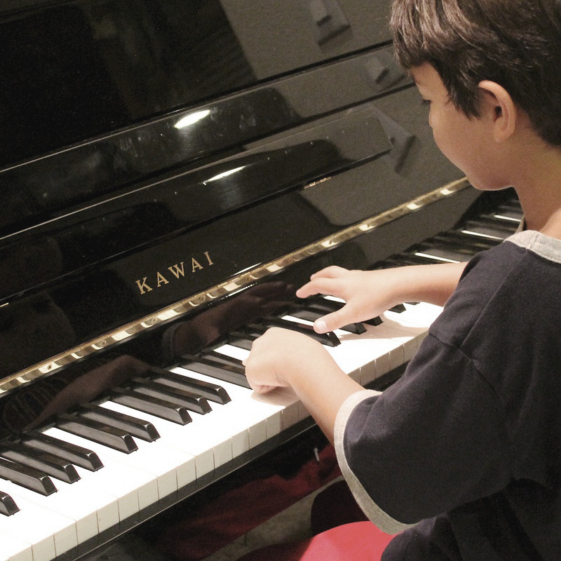 Petit garçon assis devant le piano prêt à jouer.